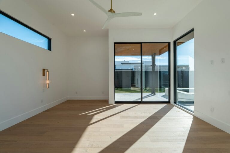 Bright, empty modern room with slim black-framed glass doors, a high horizontal window and sunlight across a wooden floor