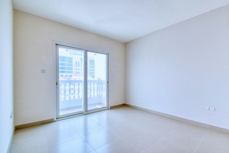 Empty room with a tiled floor and a white-framed two-panel sliding glass door leading to a balcony